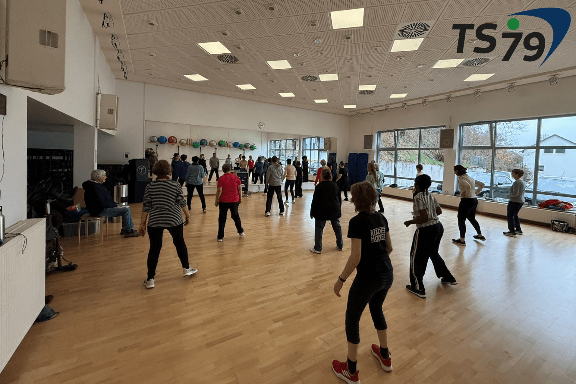 Gruppentraining in einem hellen Raum mit vielen Teilnehmern, die gemeinsam &Uuml;bungen durchf&uuml;hren.