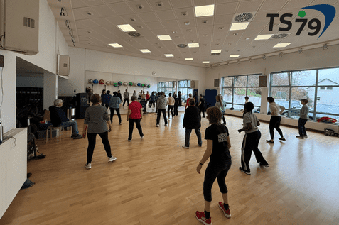 Gruppentraining in einem hellen Raum mit vielen Teilnehmern, die gemeinsam &Uuml;bungen durchf&uuml;hren.