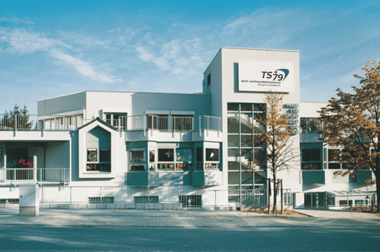 Modernes Geb&auml;ude der Sport- und Freizeitgemeinschaft TS79 mit gro&szlig;en Fenstern und B&auml;umen im Vordergrund.
