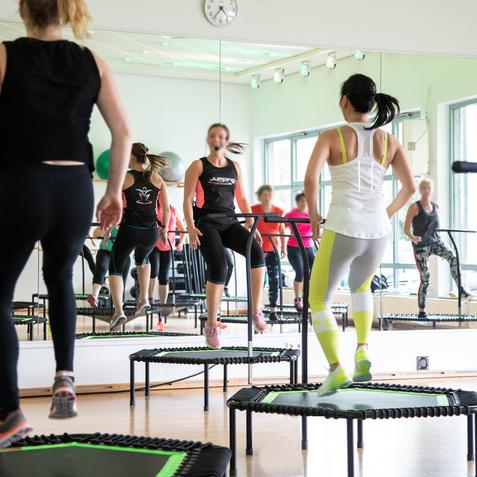 Gruppe von Frauen beim Trampolinspringen in einem Fitnessstudio vor einem Spiegel.