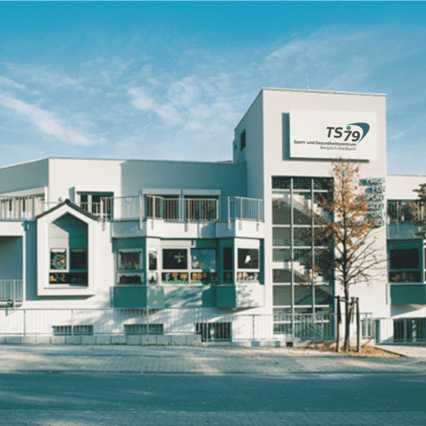 Modernes Geb&auml;ude der Sport- und Freizeitgemeinschaft TS79 mit gro&szlig;en Fenstern und B&auml;umen im Vordergrund.