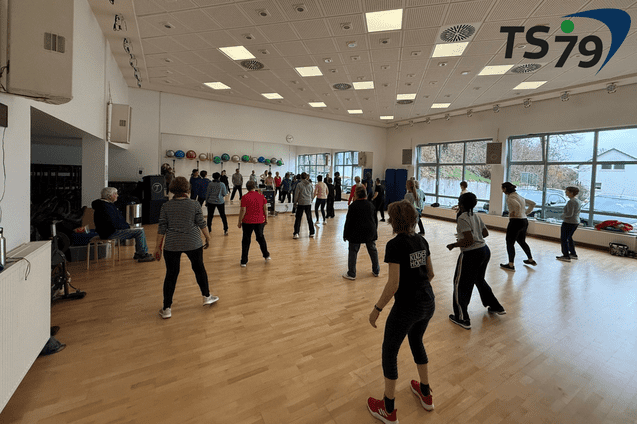 Gruppentraining in einem hellen Raum mit vielen Teilnehmern, die gemeinsam &Uuml;bungen durchf&uuml;hren.