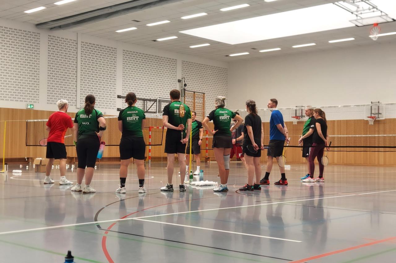 Gruppe von Badmintonspielern in Sportkleidung beim Training in einer Sporthalle mit verschiedenen Ger&auml;ten.