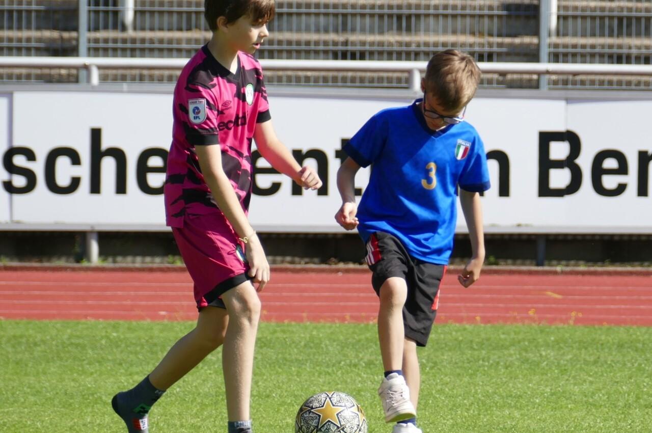 Zwei Jungen spielen auf einem Fu&szlig;ballfeld mit einem Ball, einer in pinkem Trikot, der andere in blau mit Shorts.