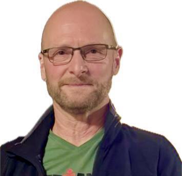 Ein Mann mit Brille und kurz geschorenem Kopf tr&auml;gt ein gr&uuml;nes T-Shirt und h&auml;lt einen Pokal in der Hand.