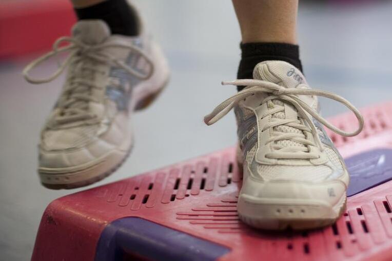 F&uuml;&szlig;e in Sportschuhen stehen auf einem roten Step-Brett in einem Fitnessraum mit blassem Boden.