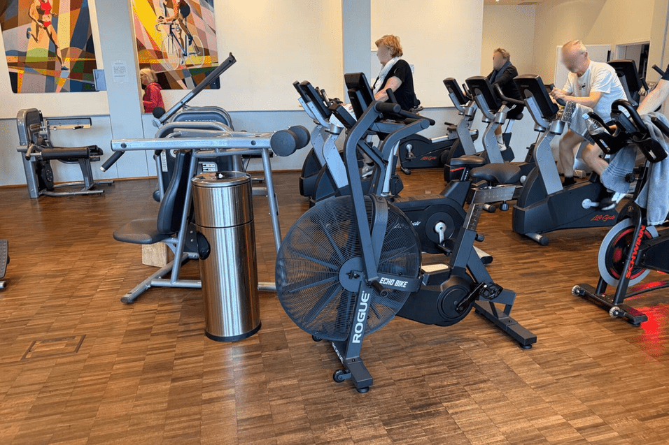 Fitnessstudio mit verschiedenen Geräten, darunter ein Luftbike, Krafttrainingsgeräte und Ausdauergeräte im Hintergrund.