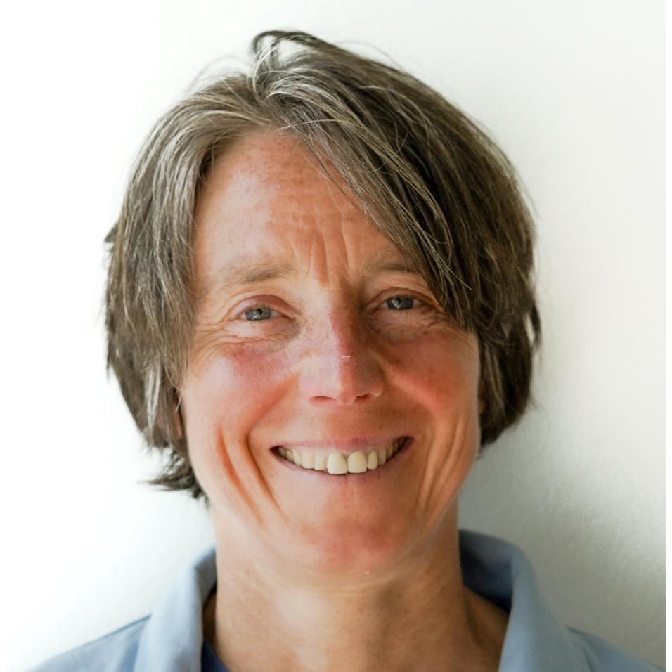 Porträt einer lächelnden Frau mit kurzer, grauer Haarfrisur, die einen blauen Kragenpullover trägt.