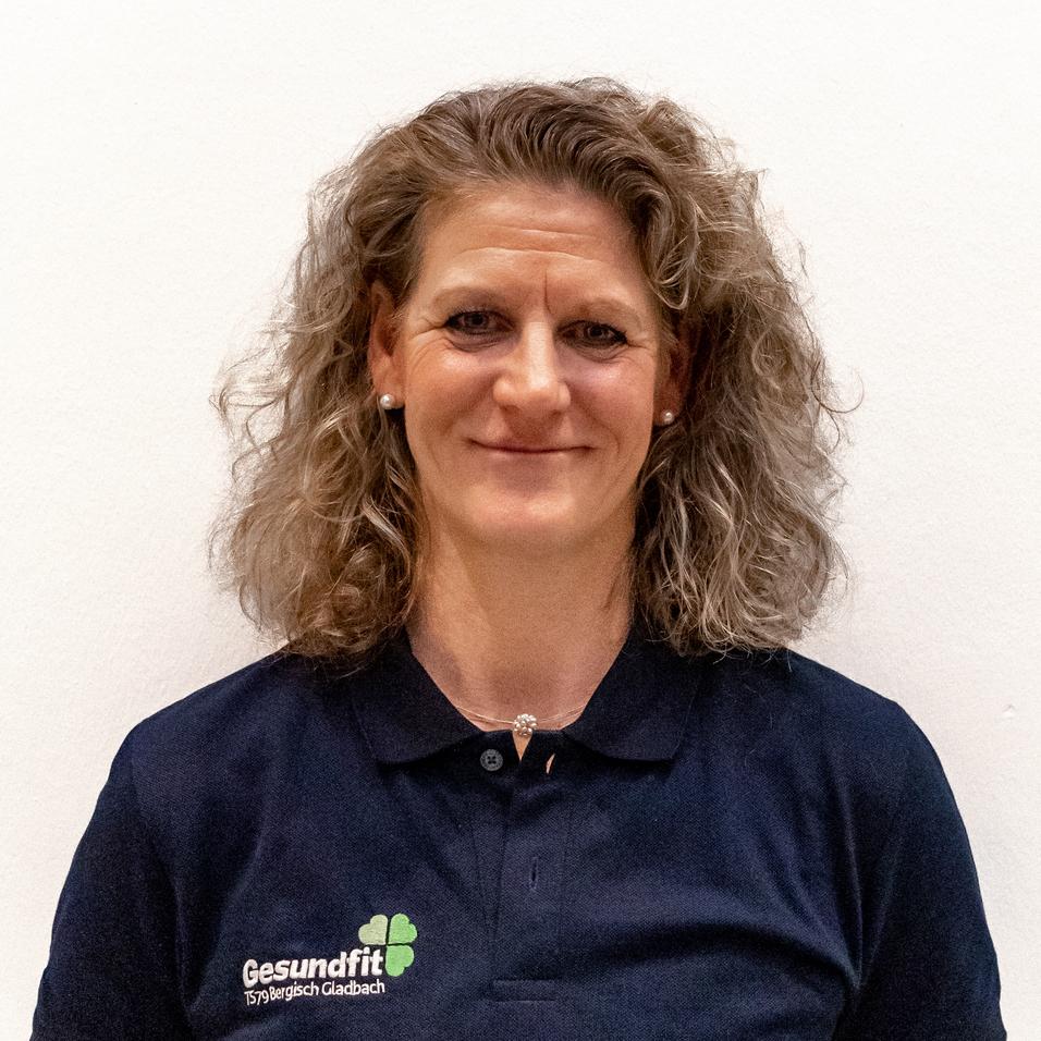 Porträt einer lächelnden Frau mit lockigem Haar, getragen in einem dunkelblauen Poloshirt mit Logo. Weißer Hintergrund.