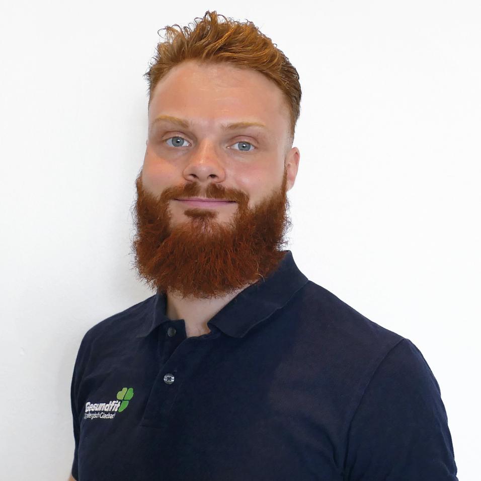 Mann mit vollem, roten Bart und blonden Haaren trägt ein schwarzes Poloshirt vor weißem Hintergrund.