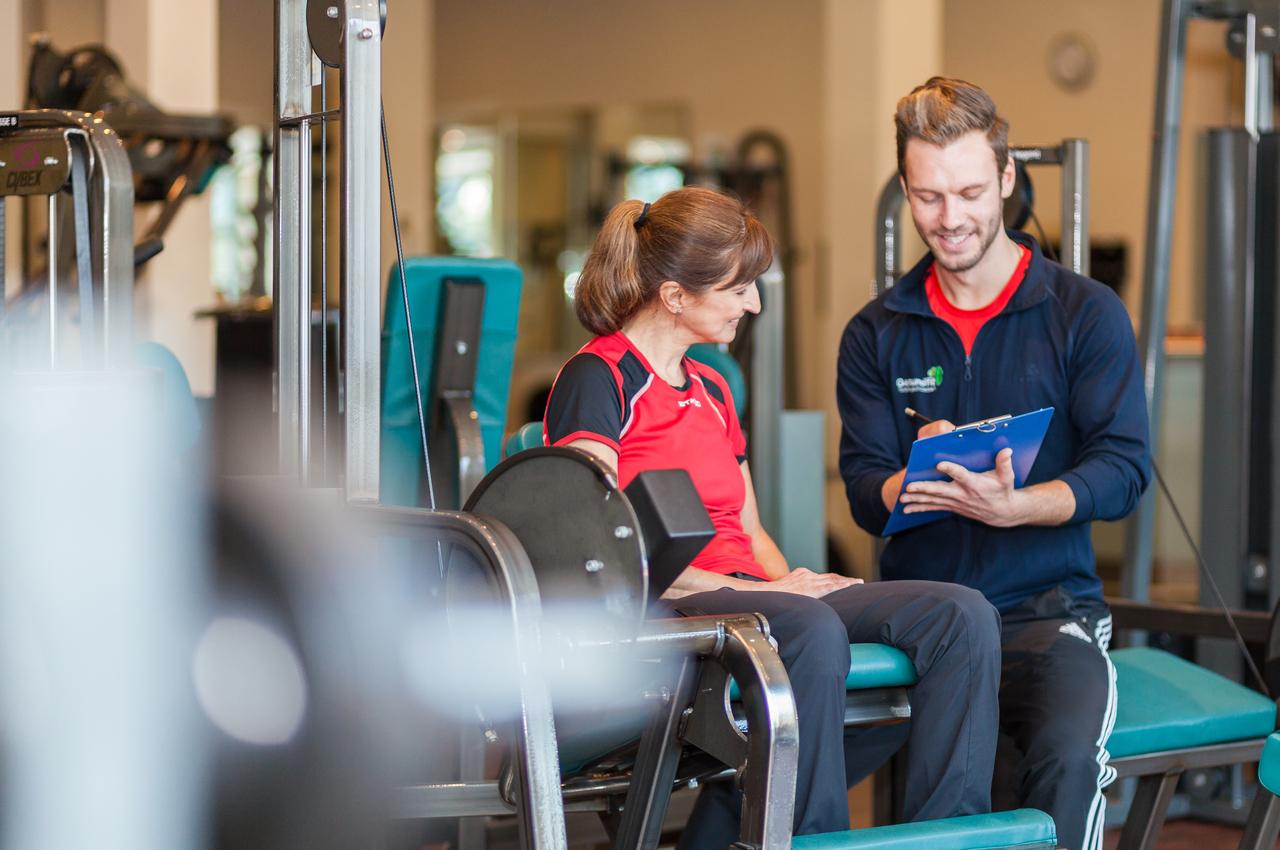 Ein Trainer ber&auml;t eine Frau am Fitnessger&auml;t in einem modernen Fitnessstudio.