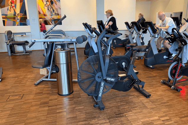 Fitnessstudio mit verschiedenen Geräten, darunter ein Luftbike, Krafttrainingsgeräte und Ausdauergeräte im Hintergrund.