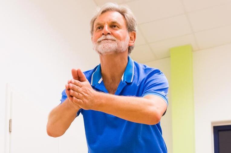 Zwei Personen trainieren auf Trampolinen in einem hellen &Uuml;bungsraum, einer springt, w&auml;hrend der andere in der Mitte h&auml;lt.