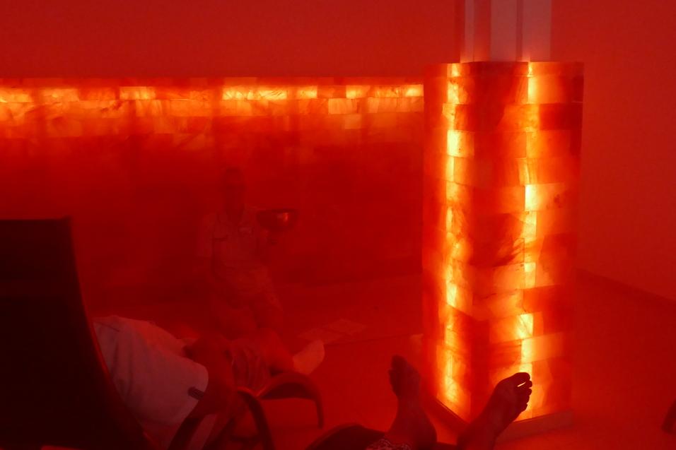 Ruhebereich mit r&ouml;tlicher Beleuchtung, Salzsteinwand und Personen in bequemen Liegen.