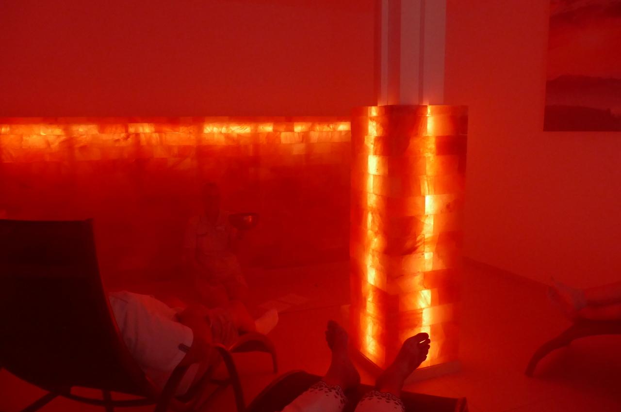 Ruhebereich mit r&ouml;tlicher Beleuchtung, Salzsteinwand und Personen in bequemen Liegen.