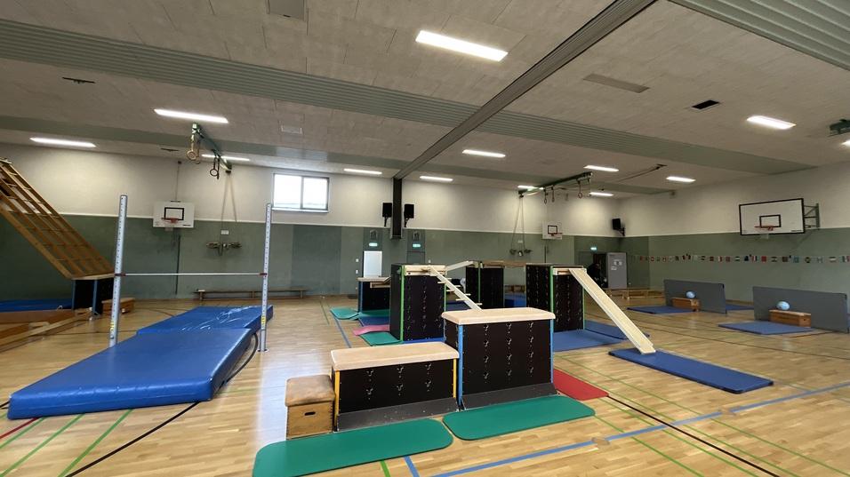 Sporthalle mit verschiedenen Turnger&auml;ten, Matten und einer Rutsche auf einem hellen Holzboden.