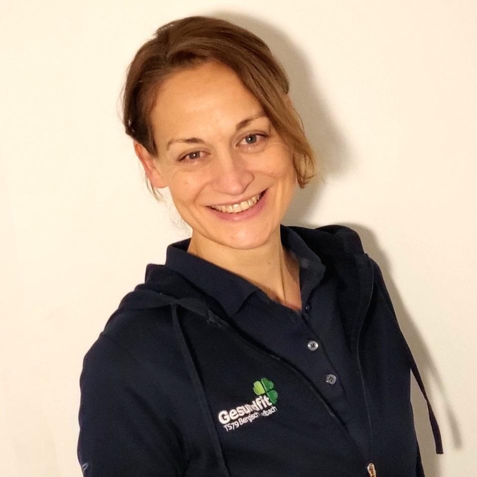 Frau mit braunen Haaren lächelt in einem dunkelblauen Hoodie vor neutralem Hintergrund.