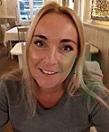 Lächelnde Frau mit blonden Haaren sitzt in einem Restaurant, Hintergrund mit Tischen und warmem Licht.