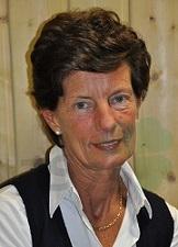 Portr&auml;t einer Frau mit kurzen, braunen Haaren, die in einem schwarz-wei&szlig;en Outfit vor einer hellen Holzwand sitzt.