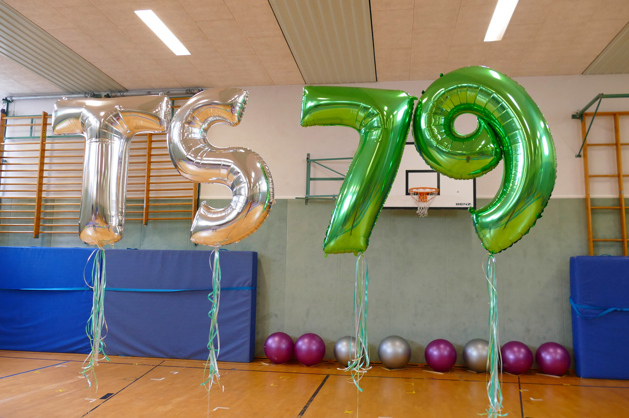 Ballons mit den Zahlen "TS79" und "79" in Silber und gr&uuml;n stehen in einer Sporthalle vor einem blauen Ger&auml;t.