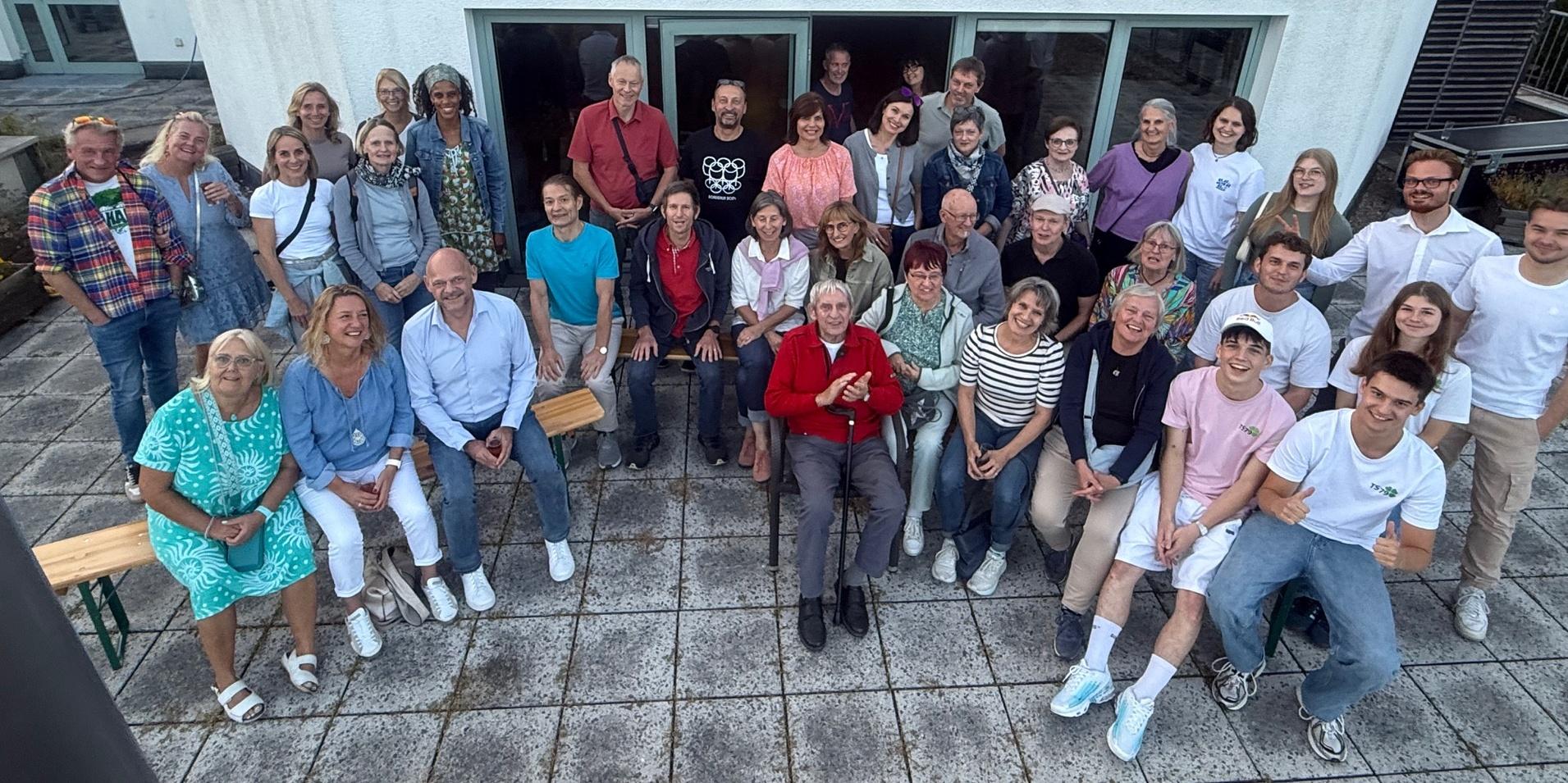 Gruppenfoto von 42 Personen auf einer Terrasse vor einem modernen Geb&auml;ude, l&auml;chelnd und in entspannter Atmosph&auml;re.