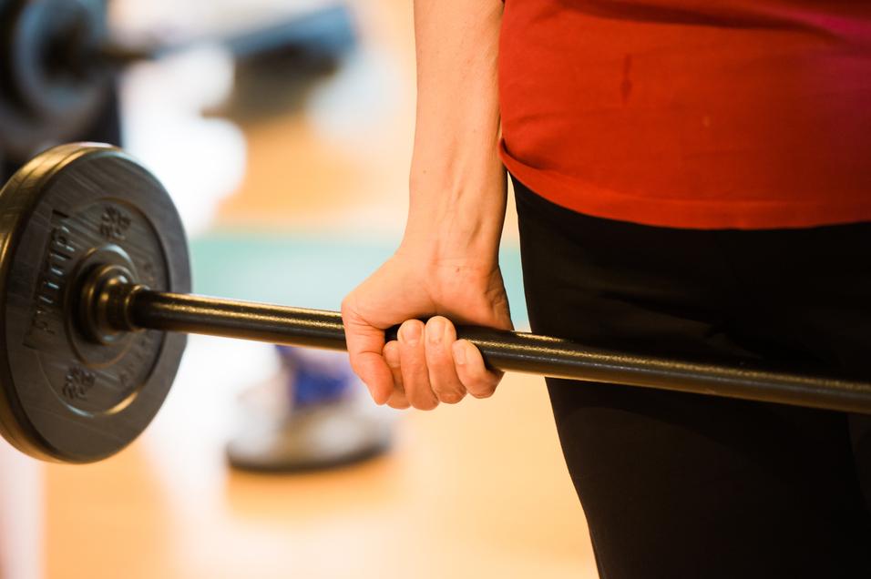 Nahaufnahme einer Hand, die eine Langhantel mit Gewichten in einem Fitnessstudio hält.