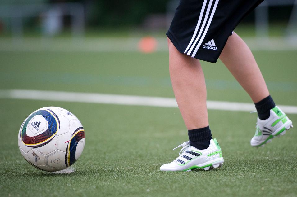 Ein Fuß mit Fußballschuhen tritt auf einen Fußball auf einem Kunstrasenfeld.
