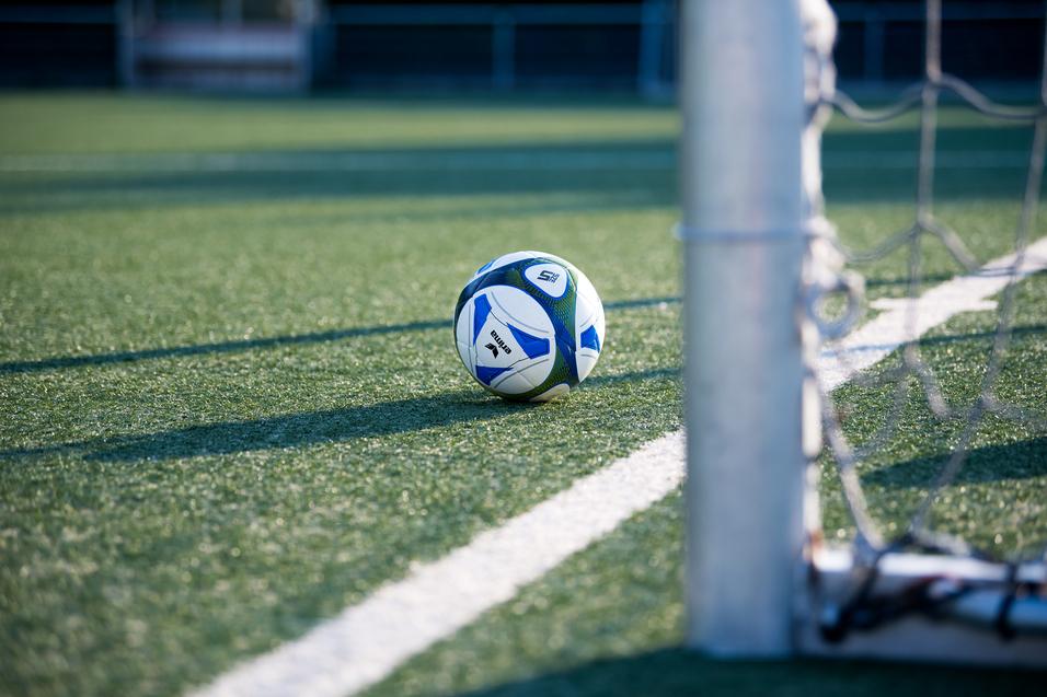 Fußball liegt auf einem Kunstrasenplatz, nahe einem Torpfosten mit Netz.